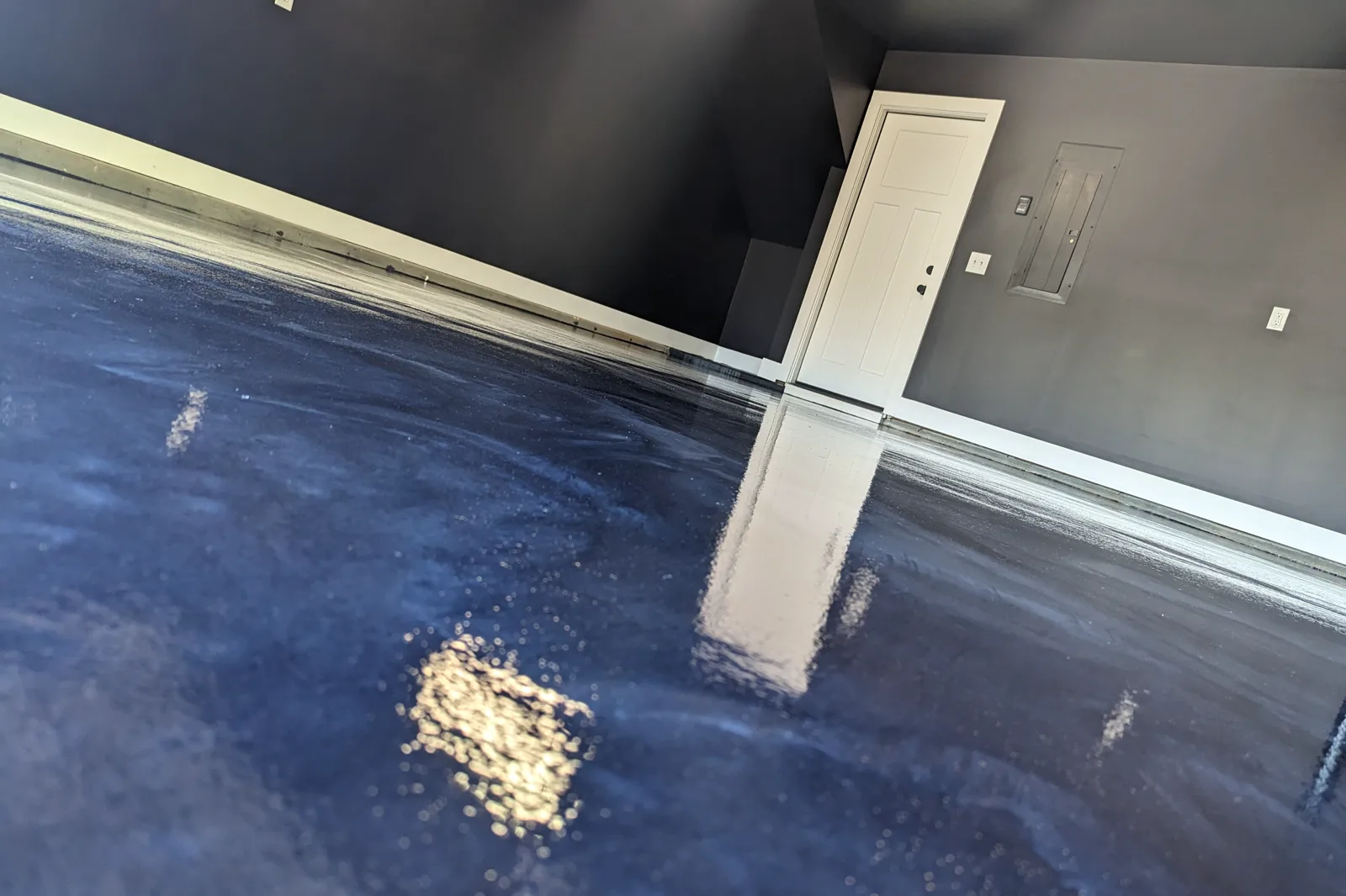 A finished blue and silver metallic garage floor with a high-gloss surface reflecting a doorway and the light above it.