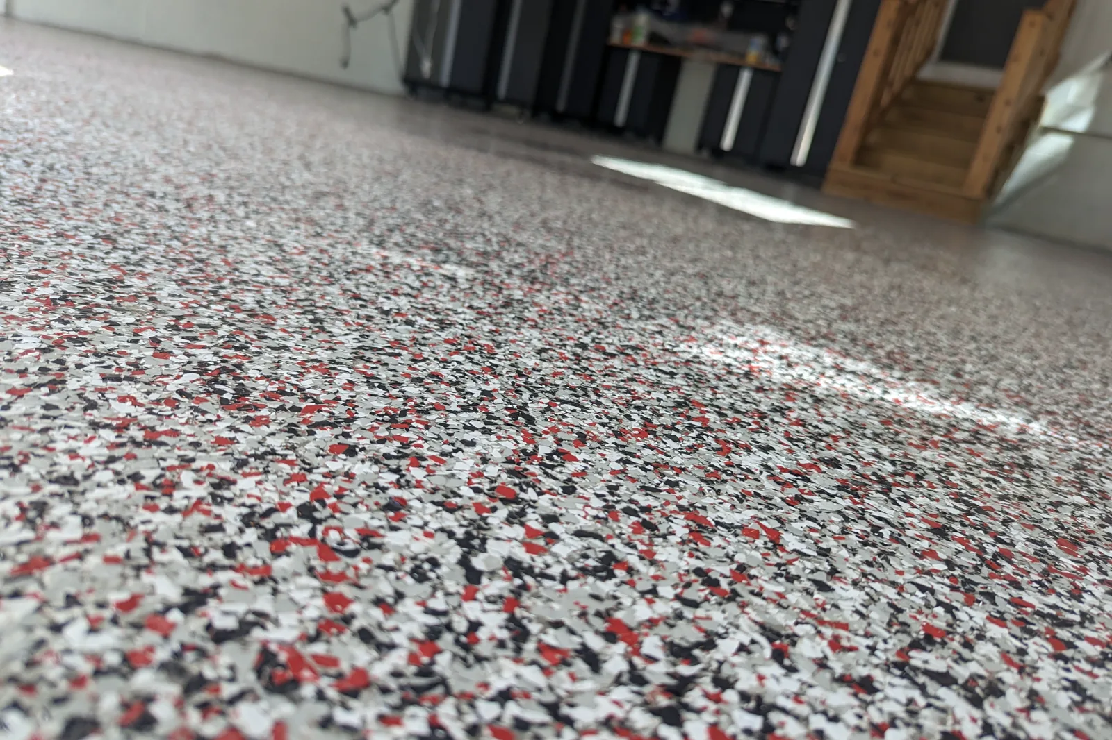 A low-angle view of a finished garage floor in a custom flake blend of red, white, black, and gray, with storage cabinets in the background.