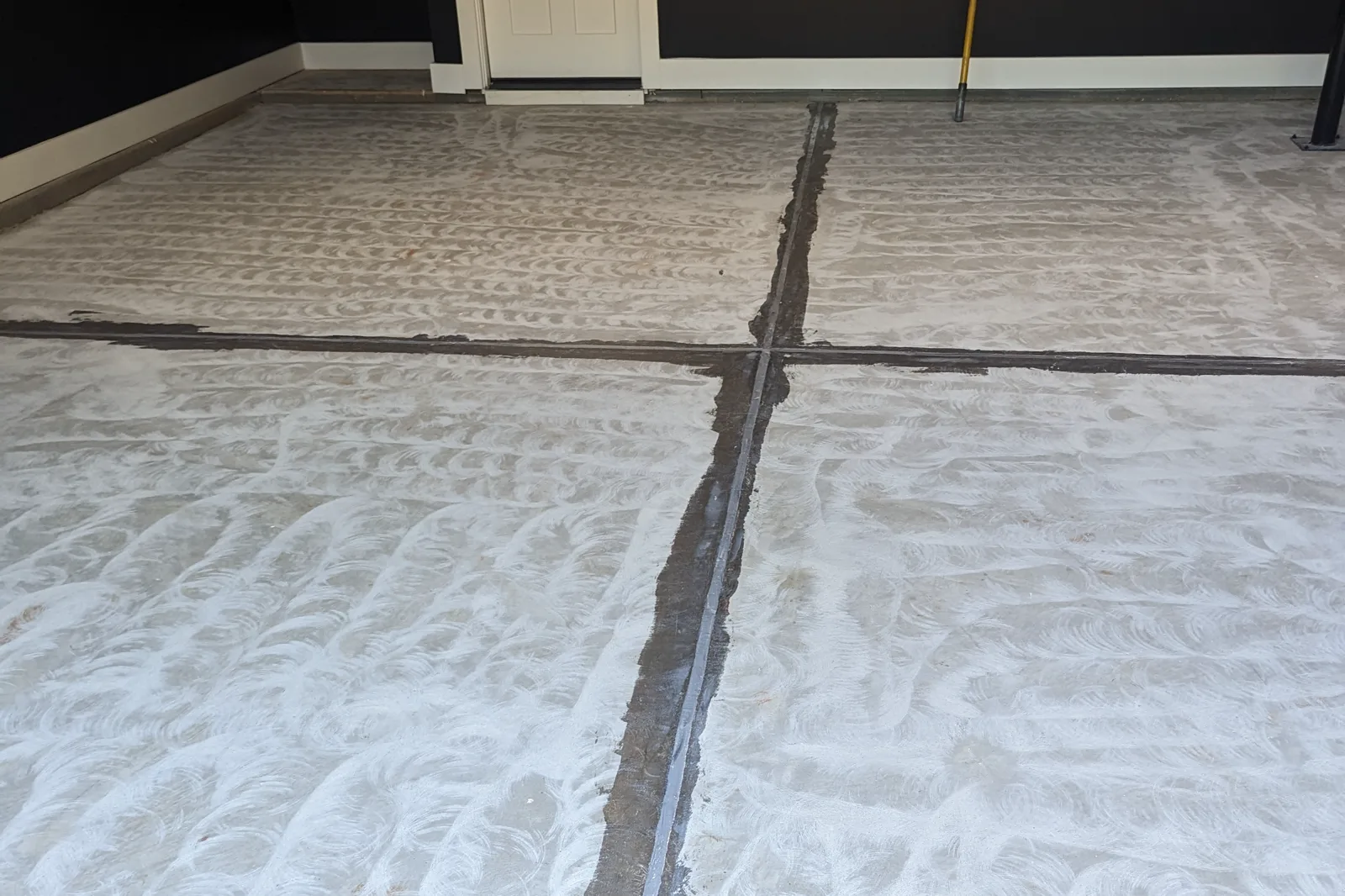 A ground concrete slab with its control joints filled and troweled flush, ready for coating, with the grinder pattern still visible across the surface.