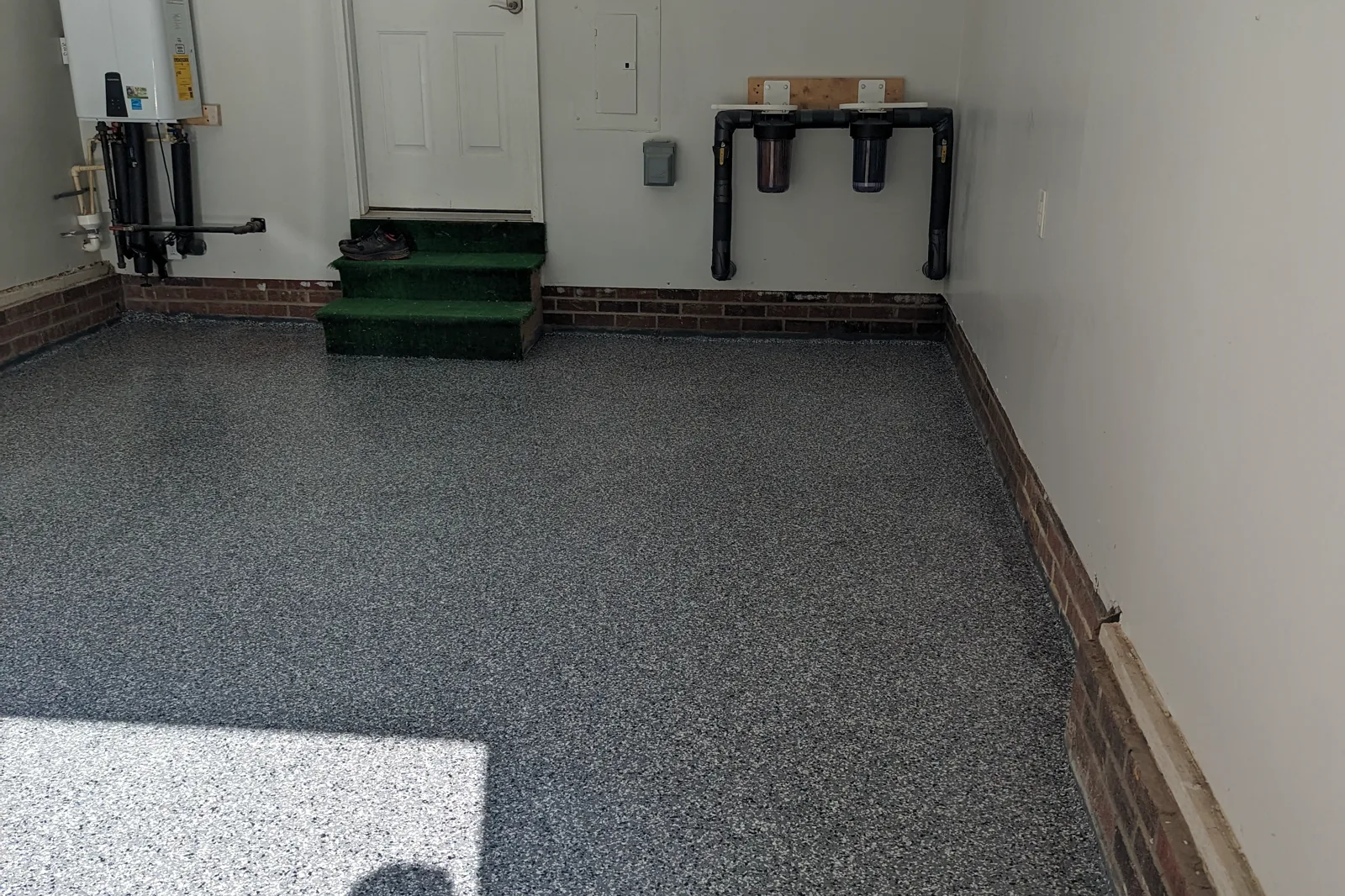 A completed gray flake garage floor, clean and entirely empty, with the coating carried up to a brick knee wall.