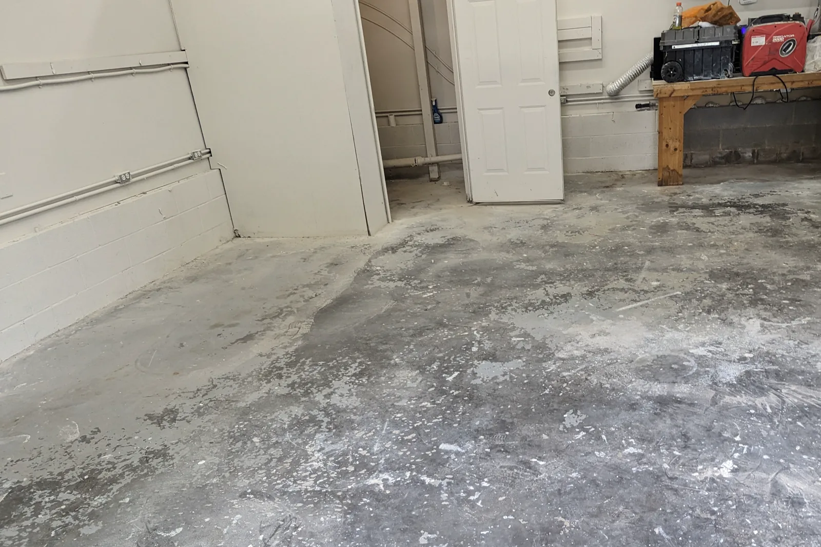 A garage floor before any work has started, showing a stained and patchy concrete slab with remnants of old surface material.