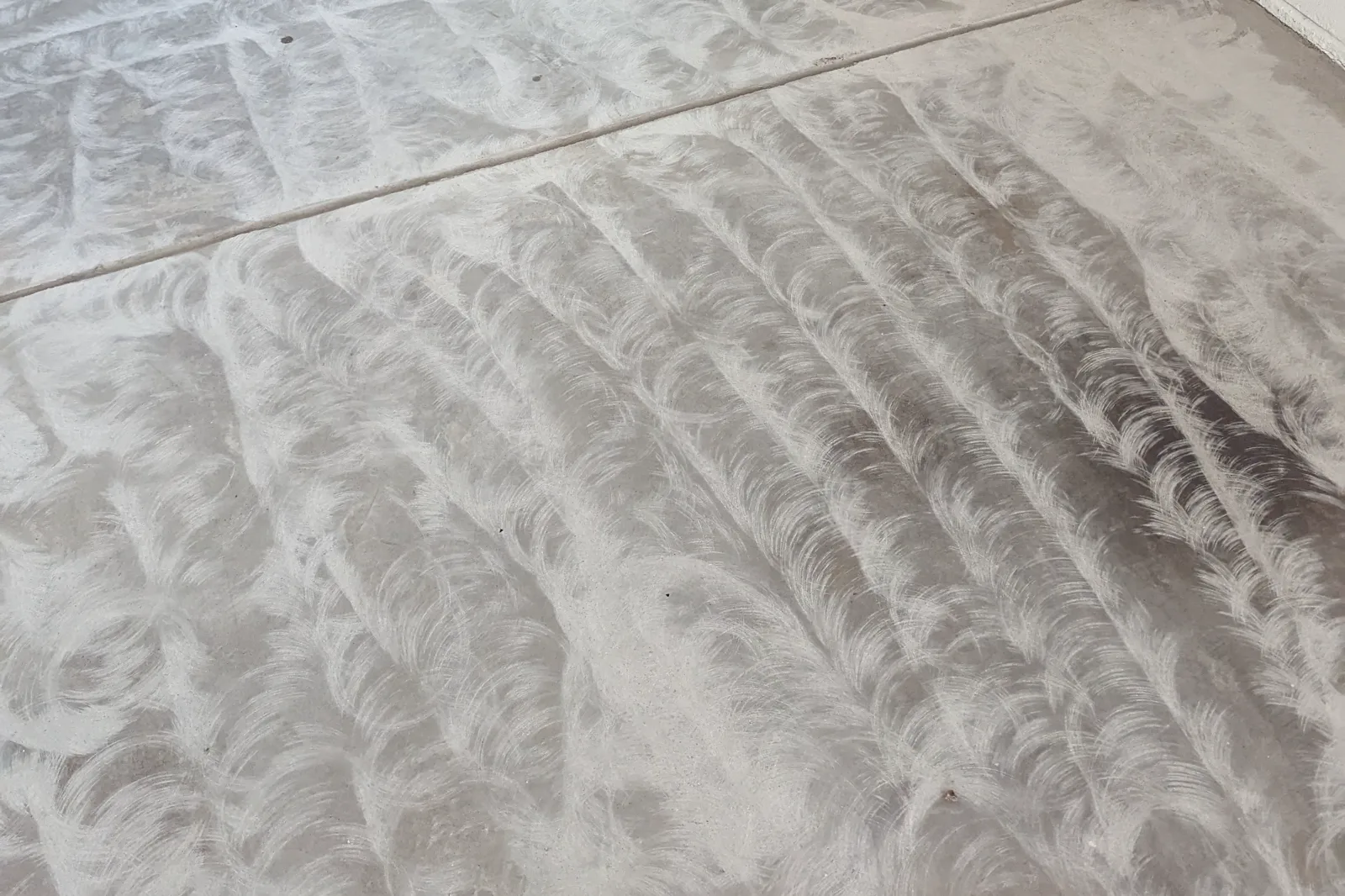 A garage slab after diamond grinding, covered in the overlapping circular pattern left by the grinder heads, with a control joint running across it.