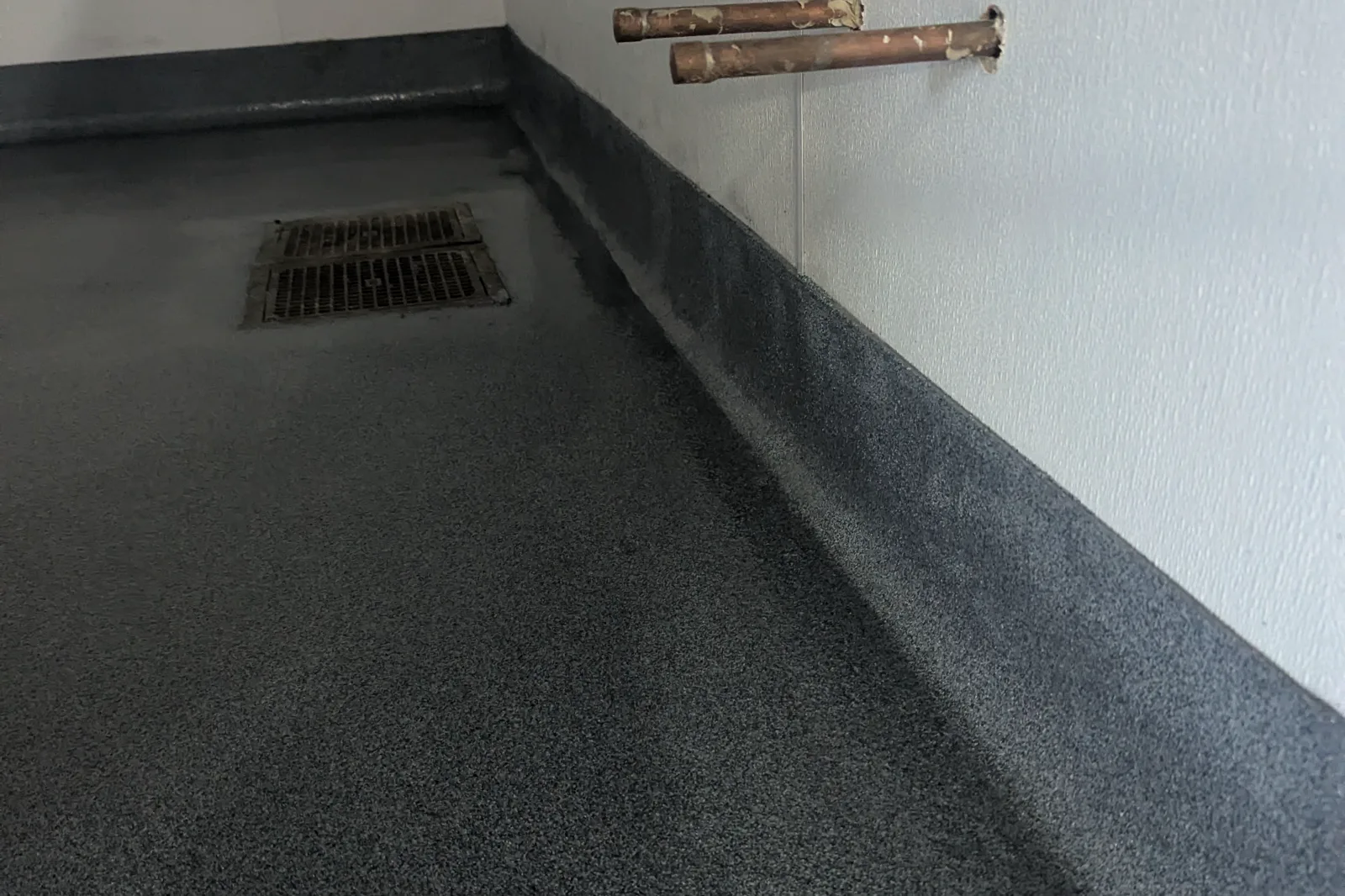 A commercial service room with a dark textured floor carried up the wall as an integral coved base, with a floor drain set into the surface.