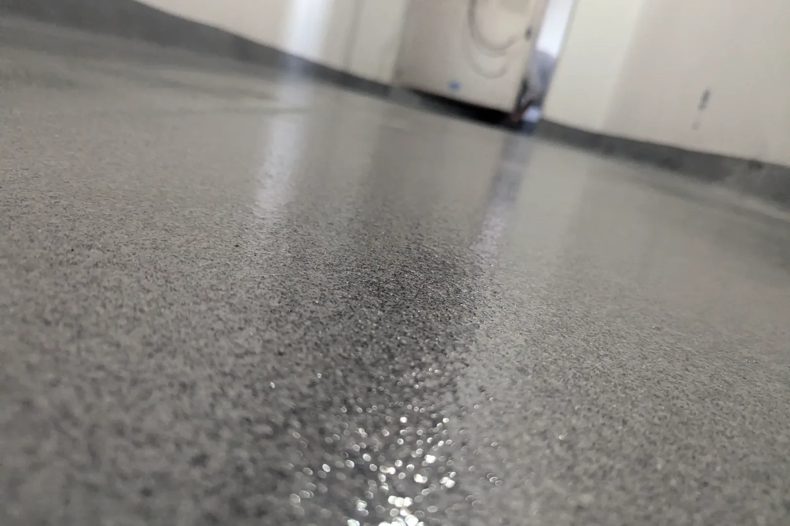 Low-angle macro of a broadcast floor surface sealed under a clear finish, the granular texture visible with light catching the sheen across it.