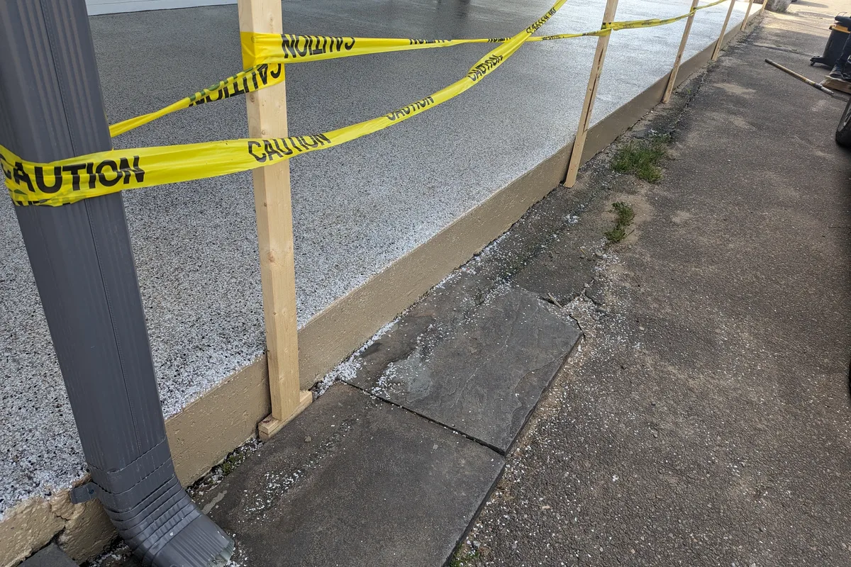 Yellow caution tape strung on temporary posts across a newly coated exterior walkway, with the finished flake surface visible behind it.