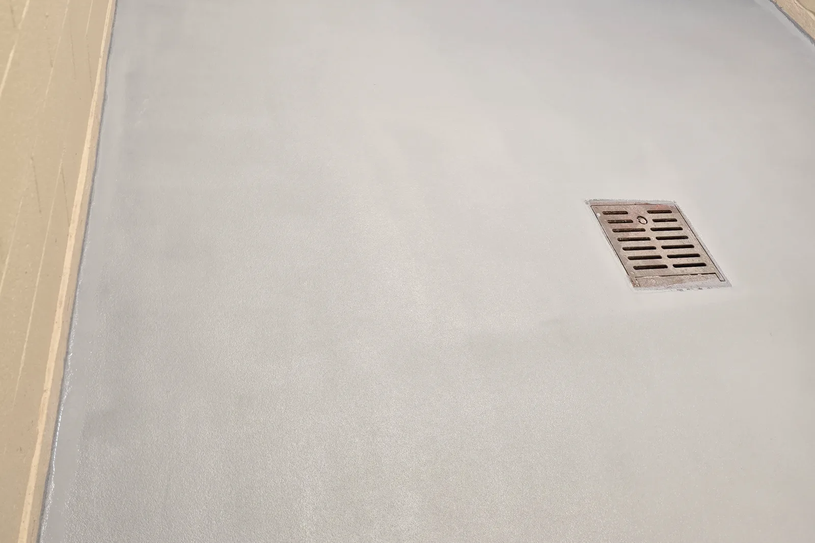 A freshly coated commercial floor, light gray with a floor drain and a coved base, left completely empty.
