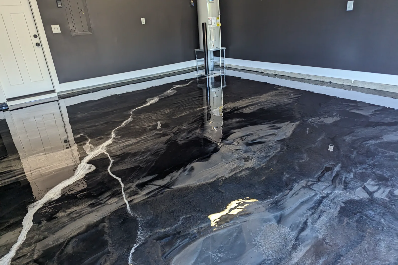 A freshly poured black and silver metallic garage floor, still liquid enough to mirror the walls, door and fittings above it.