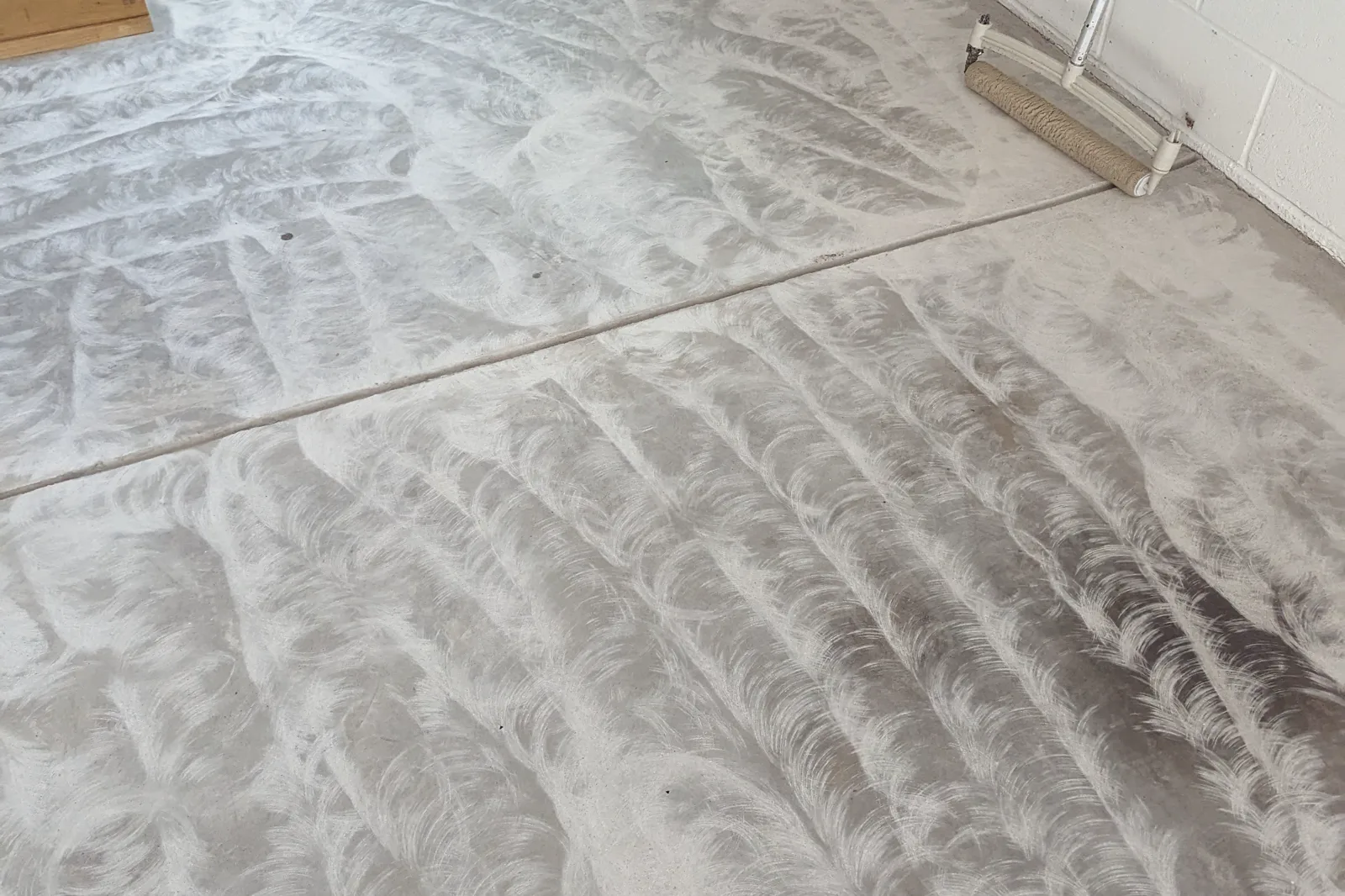 A garage slab after diamond grinding, showing the overlapping circular pattern the grinder heads leave across the concrete, with a control joint running through it.