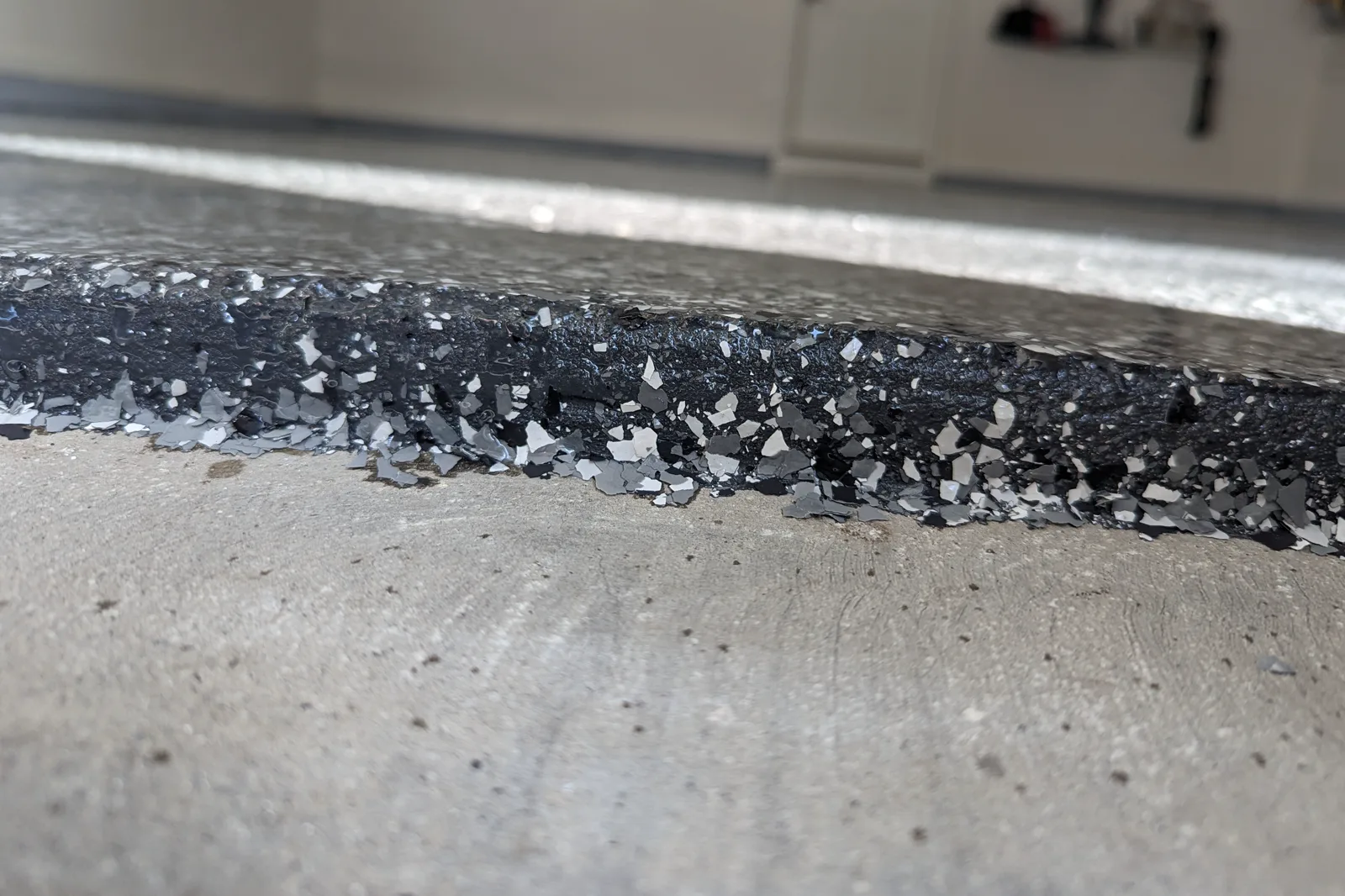 The cut edge of a finished flake floor beside bare concrete, showing the coating built up as layers with vinyl flakes suspended in resin.