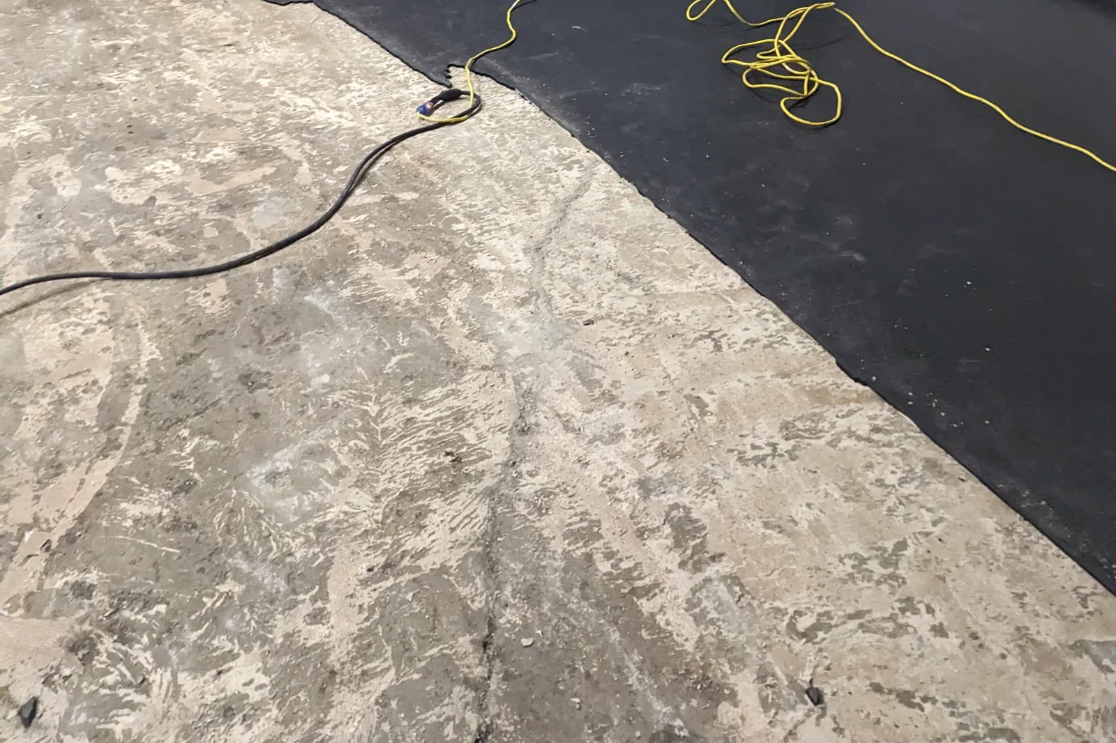 A concrete slab where sheet flooring has been pulled up, leaving adhesive and backing residue across the exposed surface next to the flooring that is still in place.