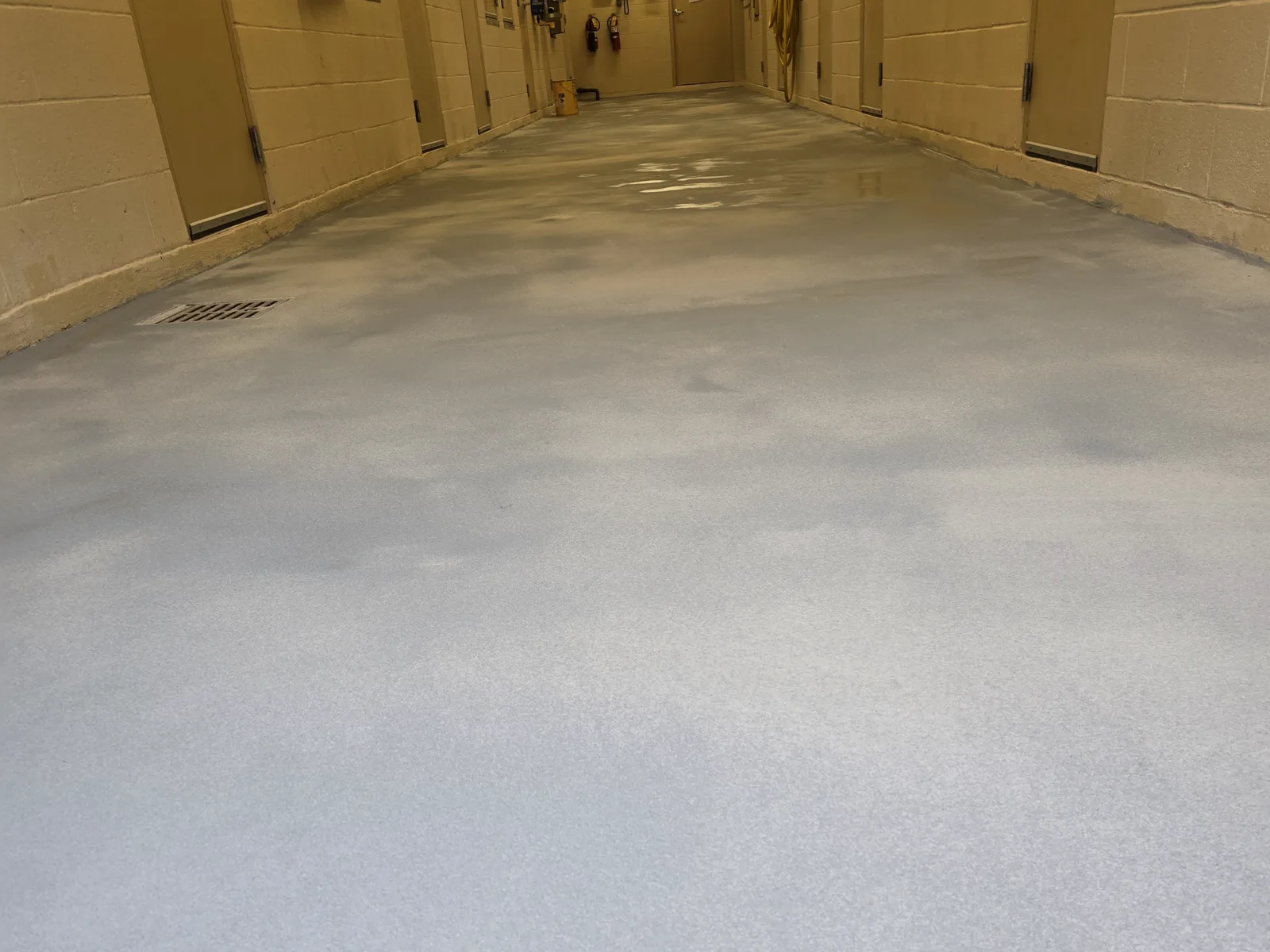 A back-of-house corridor floored with a pale grey textured coating that turns up the wall as a coved base