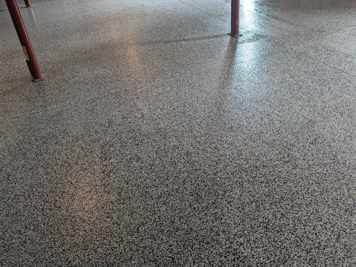 A large open floor covered in a dense grey, black and white broadcast decorative surface, running past red-painted steel columns in a building under construction.