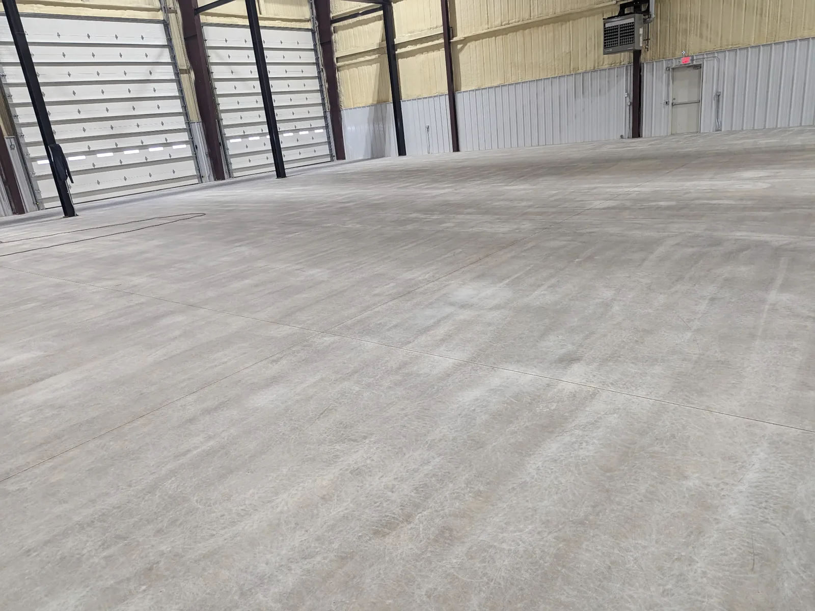 A large bare concrete slab filling an open building bay, with saw-cut joints running across it and roller doors along the far wall.