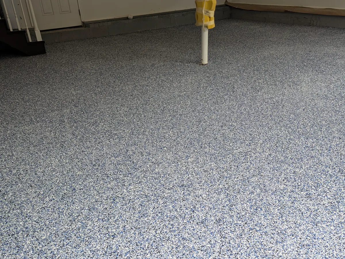 A garage floor finished in a blend of blue, white, black and grey decorative flake, running to a doorway and a set of stairs.