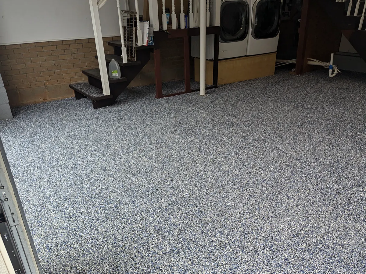 A finished garage floor covered in dense blue, white, grey and black decorative flake, with the same finish carried up a short flight of steps and running out to the garage door threshold.