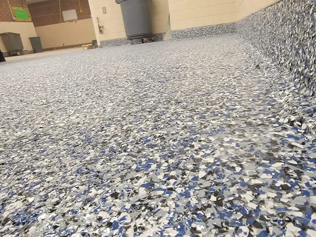 A low view across a blue, grey and white flake floor in an institutional common room, with the same flake finish carried up the wall as a coved base.