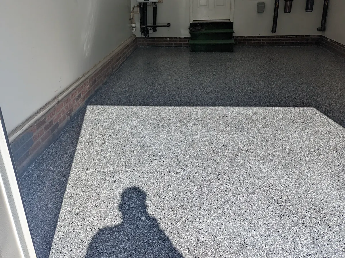 A single flake garage floor with a bright rectangle of direct sunlight falling across it from the open door, making the sunlit area look far lighter and higher in contrast than the shaded floor around it.