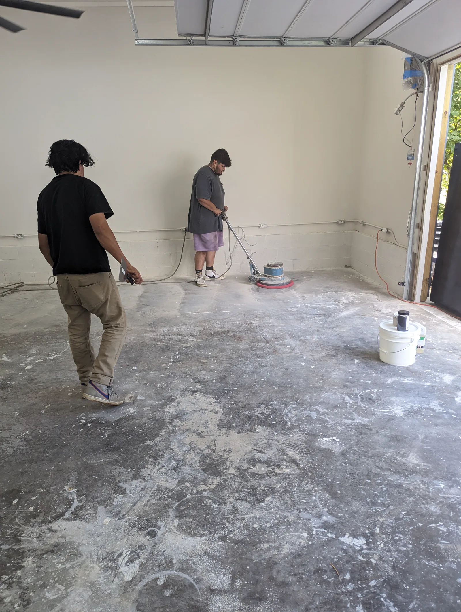 Installers preparing a garage concrete floor with a floor machine before coating