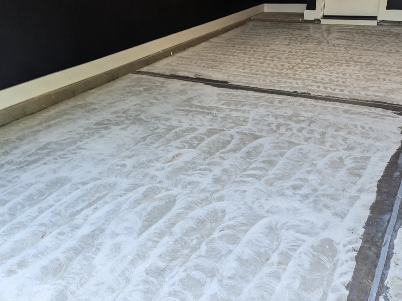 A garage slab after mechanical preparation, showing an even pattern of overlapping grinder swirls across the concrete and a treated joint running through it.