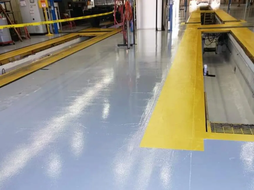 A coated aisle running between two service pits edged in yellow inside a working facility