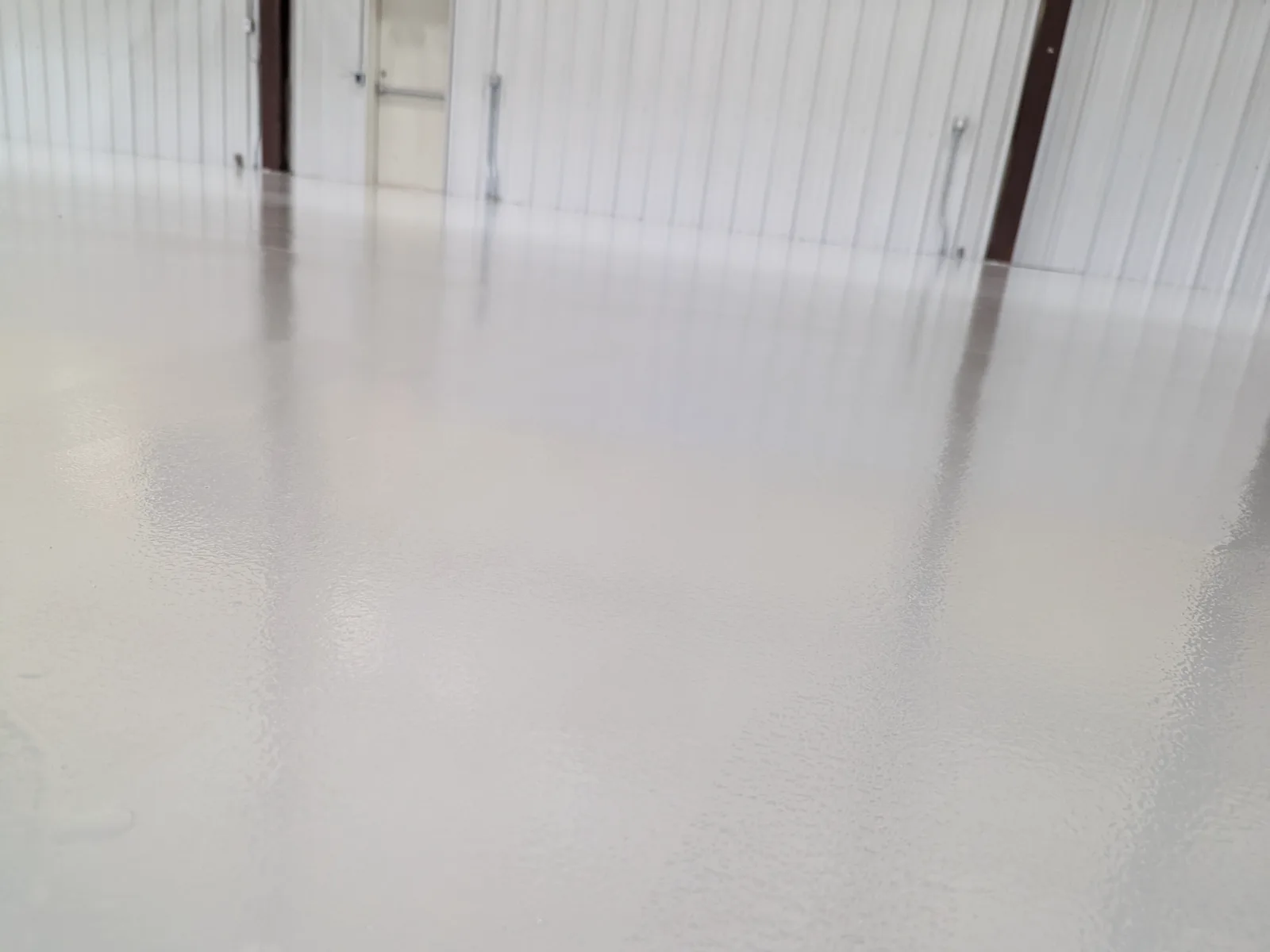 A smooth cream-coloured gloss floor running across a steel-framed building with white metal wall panels and brown structural columns.