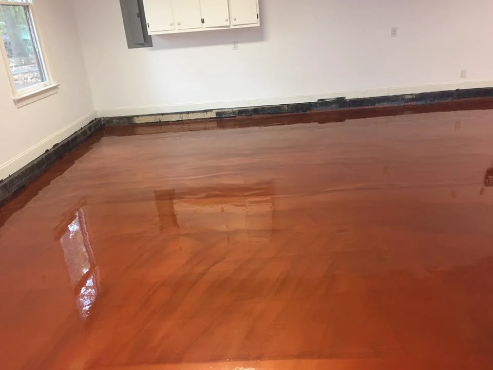 A copper-toned metallic floor filling a room with white walls and a wall cabinet, still glossy and reflecting the window light.