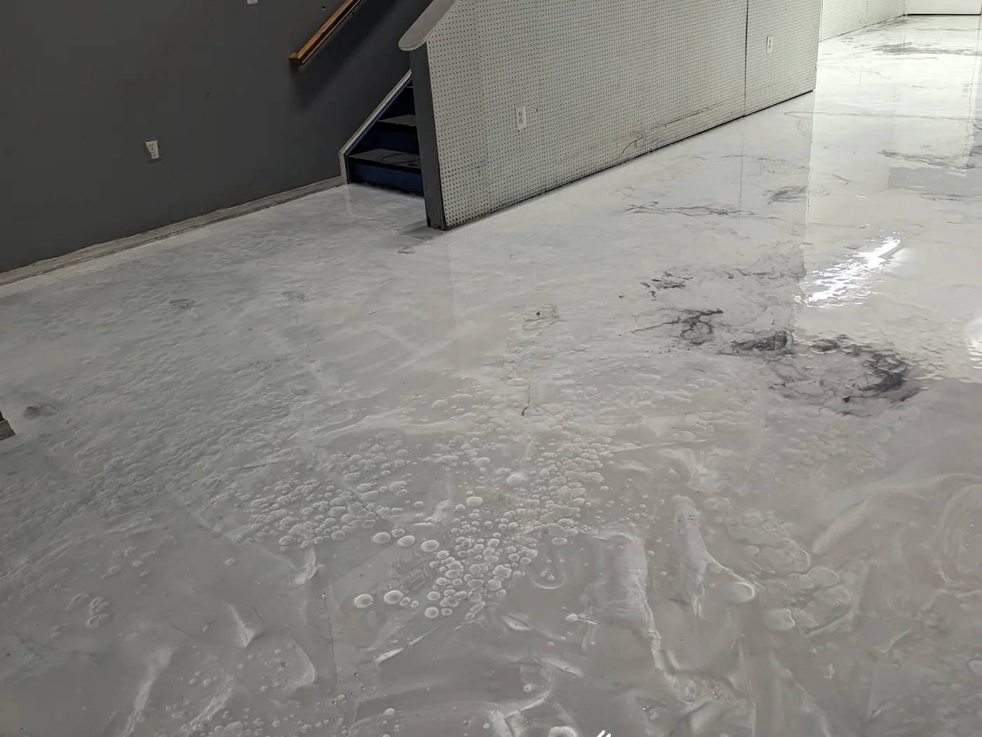A white and grey marbled metallic floor in a finished basement, with fine cell patterns and darker veining spread unevenly across the surface.