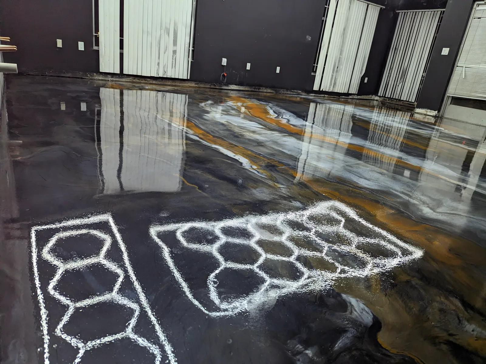 A black, grey and amber metallic floor still wet and fully reflective, with veining running across it
